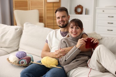 Woman teaching her boyfriend how to knit on sofa at home