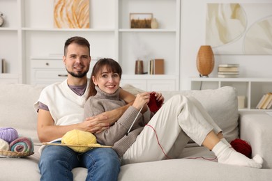 Photo of Woman teaching her boyfriend how to knit on sofa at home