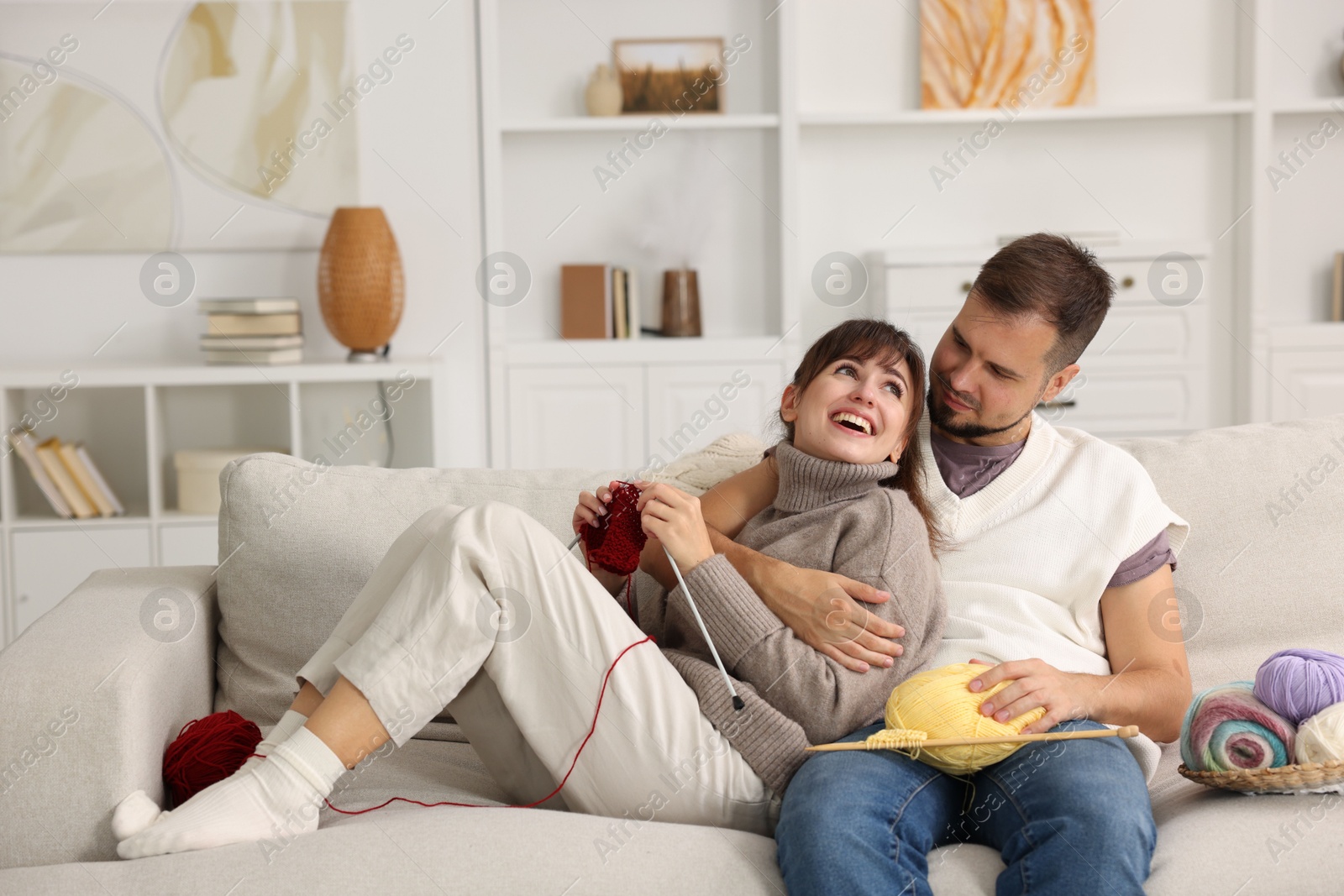 Photo of Woman teaching her boyfriend how to knit on sofa at home