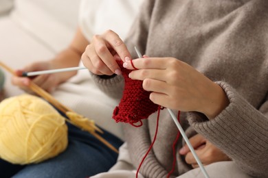 Woman teaching her boyfriend how to knit at home, closeup