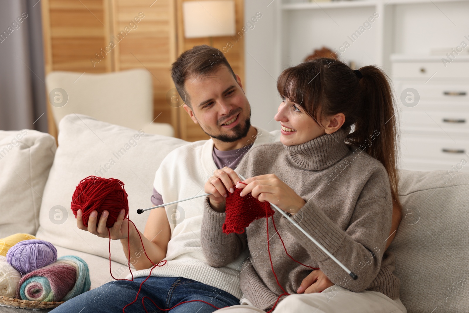 Photo of Woman teaching her boyfriend how to knit on sofa at home