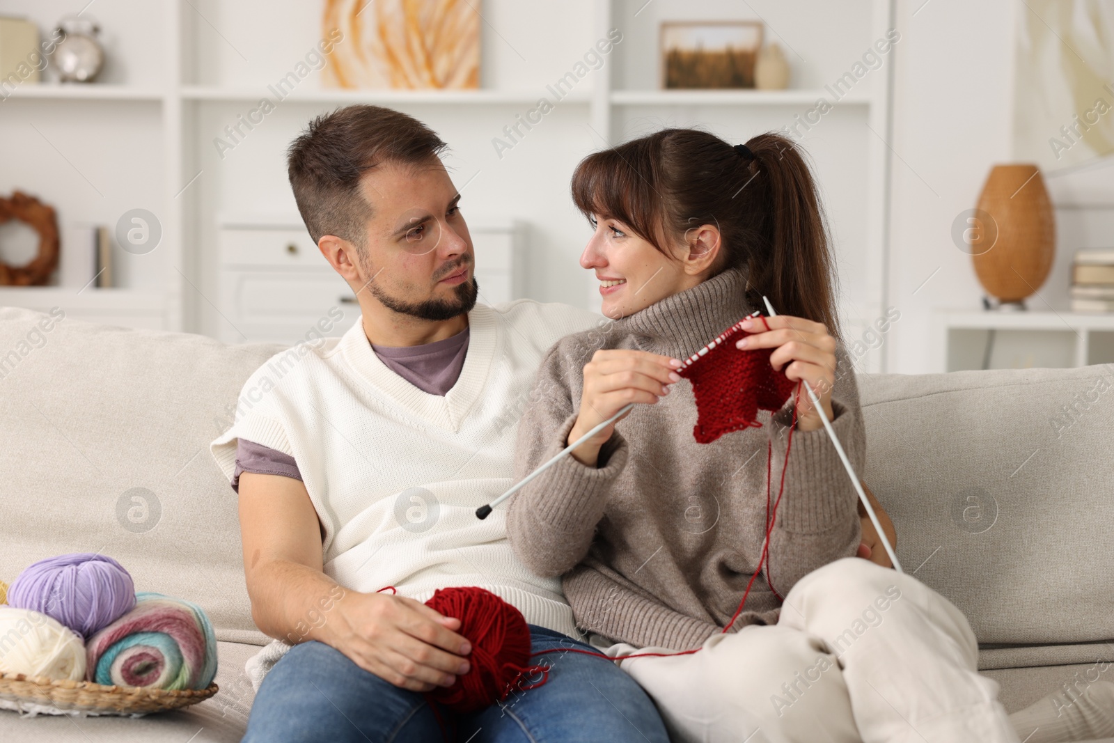 Photo of Woman teaching her boyfriend how to knit on sofa at home