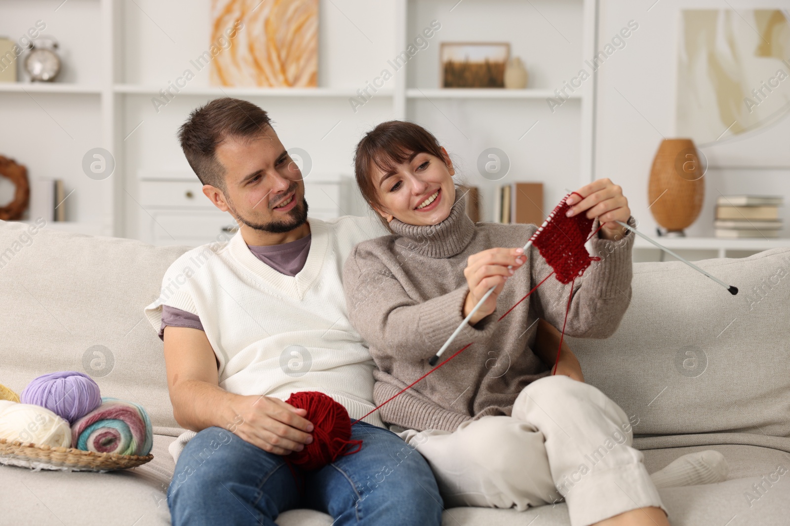 Photo of Woman teaching her boyfriend how to knit on sofa at home