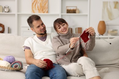 Woman teaching her boyfriend how to knit on sofa at home