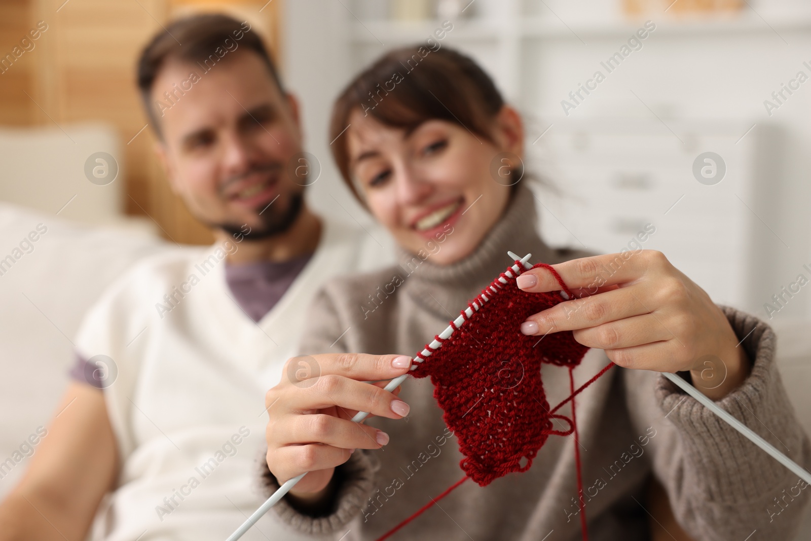 Photo of Woman teaching her boyfriend how to knit at home, selective focus