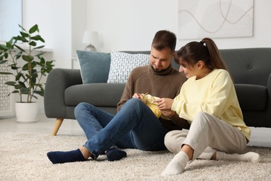 Woman teaching her boyfriend how to knit on floor at home