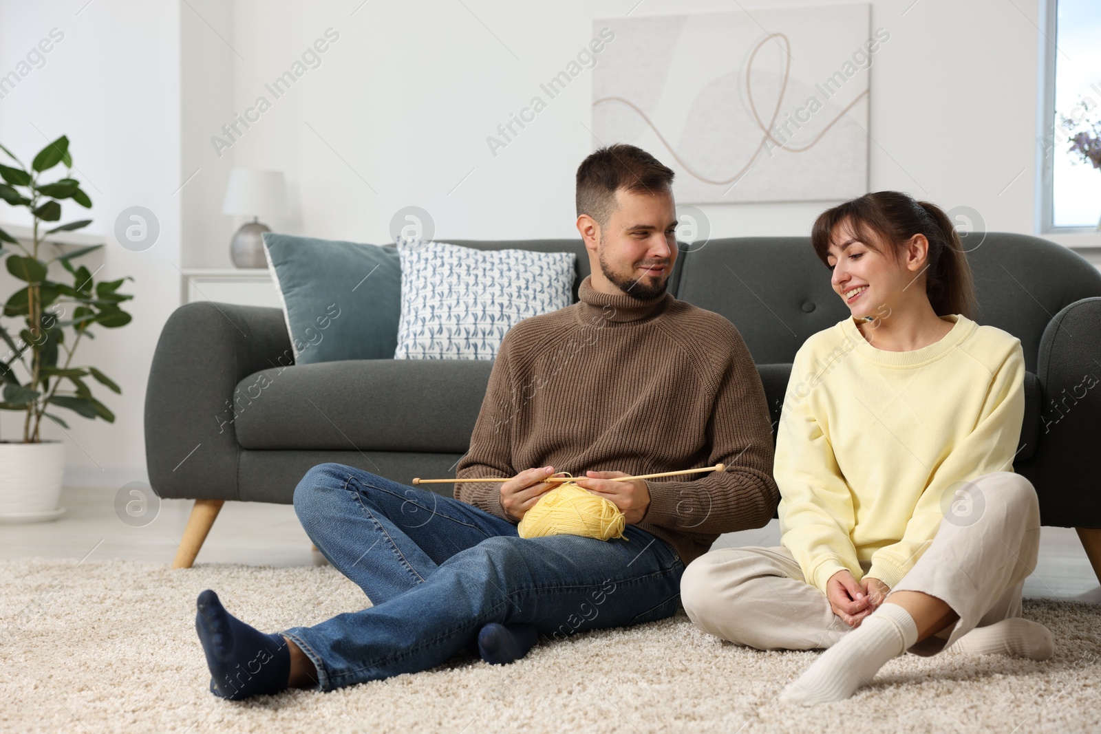 Photo of Woman teaching her boyfriend how to knit on floor at home