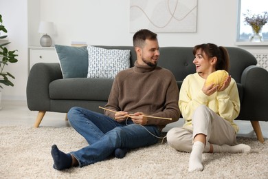 Woman teaching her boyfriend how to knit on floor at home