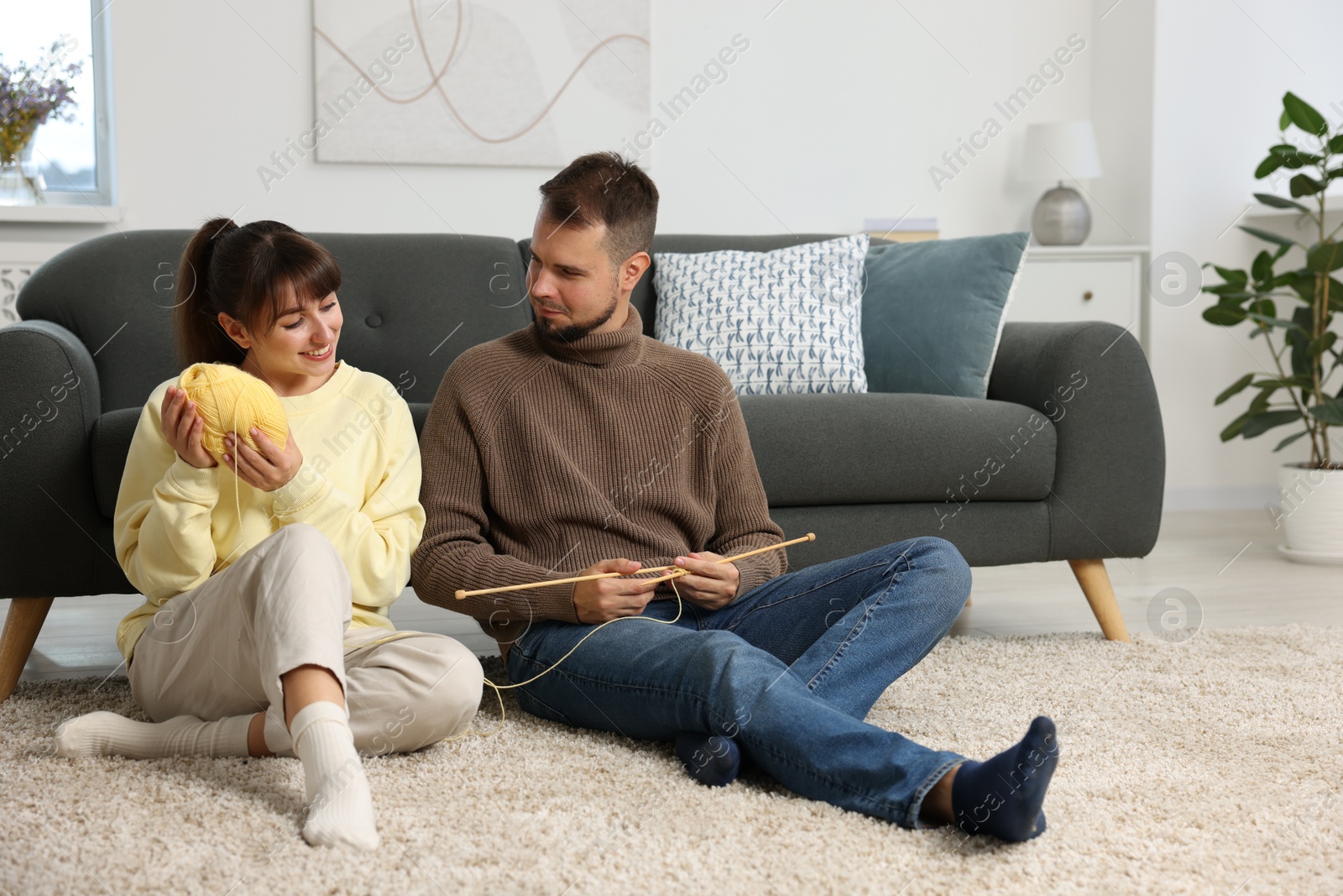 Photo of Woman teaching her boyfriend how to knit on floor at home