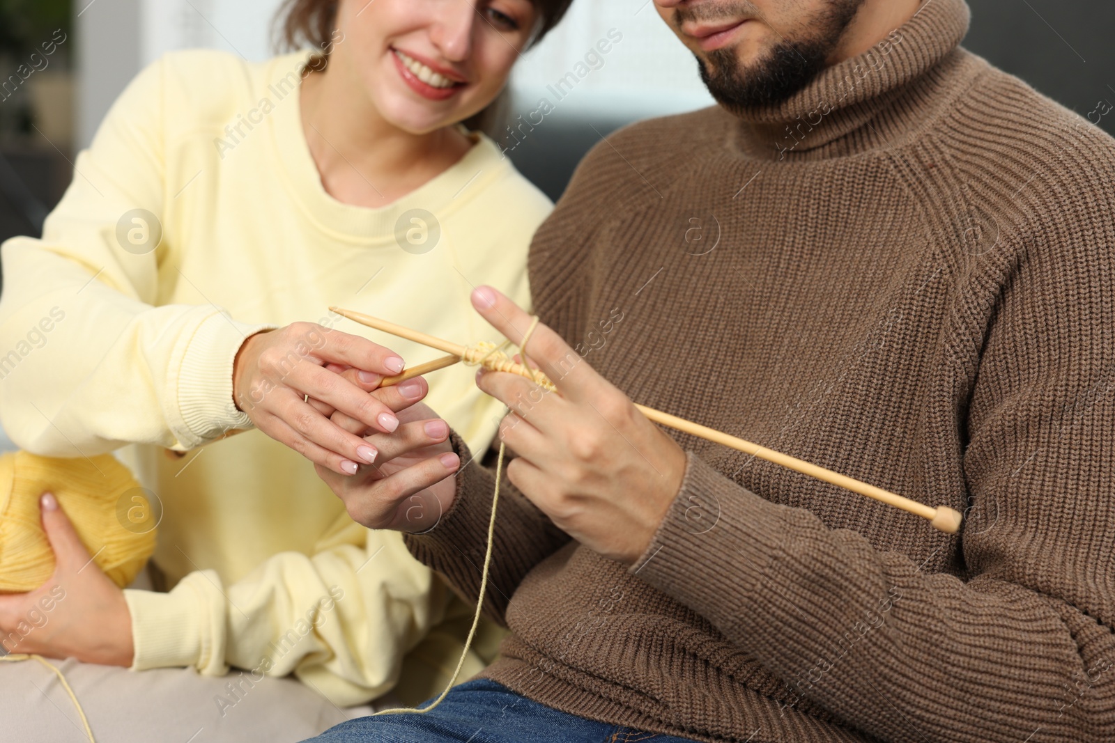 Photo of Woman teaching her boyfriend how to knit at home, closeup