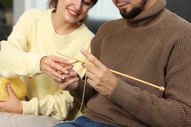 Woman teaching her boyfriend how to knit at home, closeup