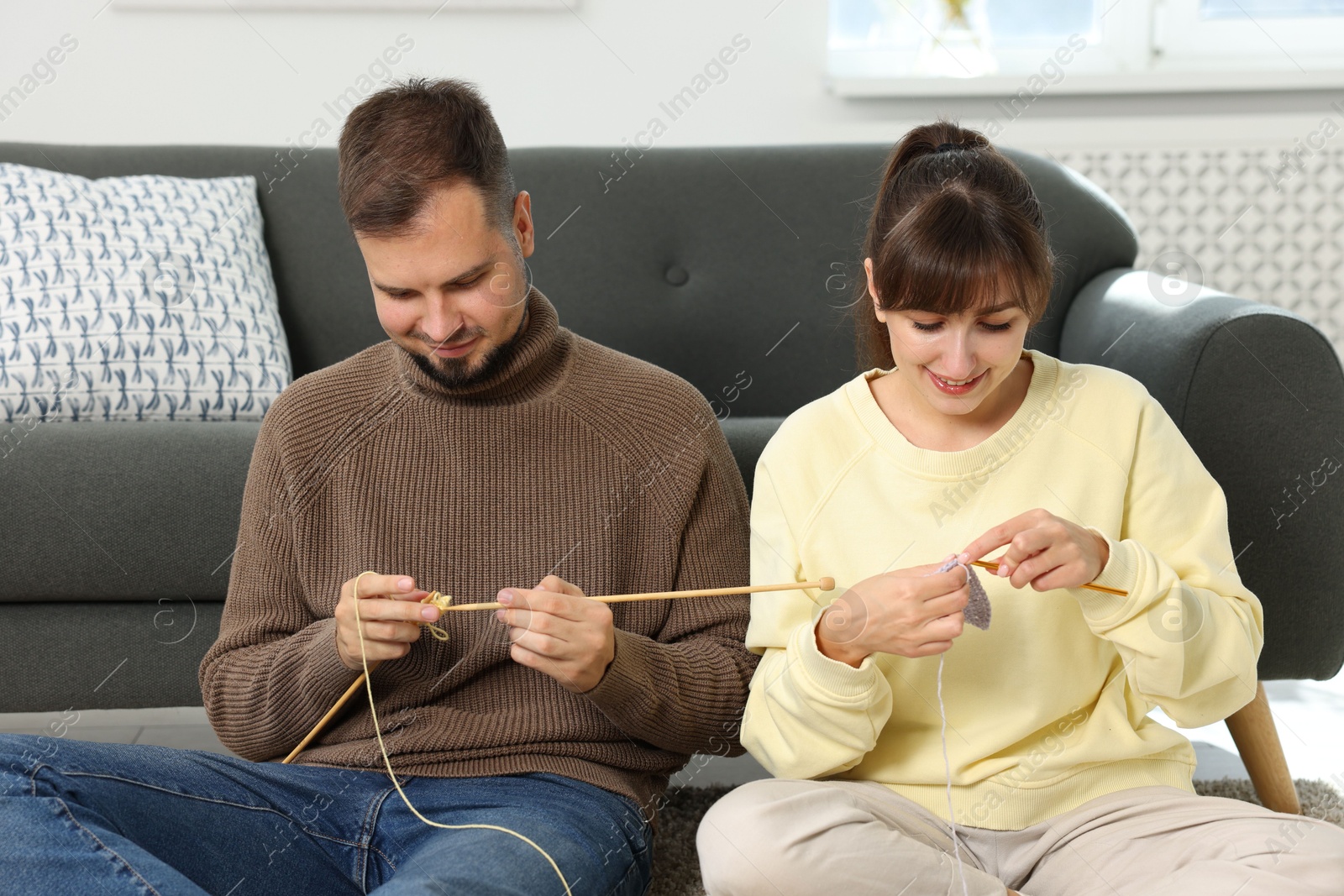 Photo of Woman teaching her boyfriend how to knit on floor at home