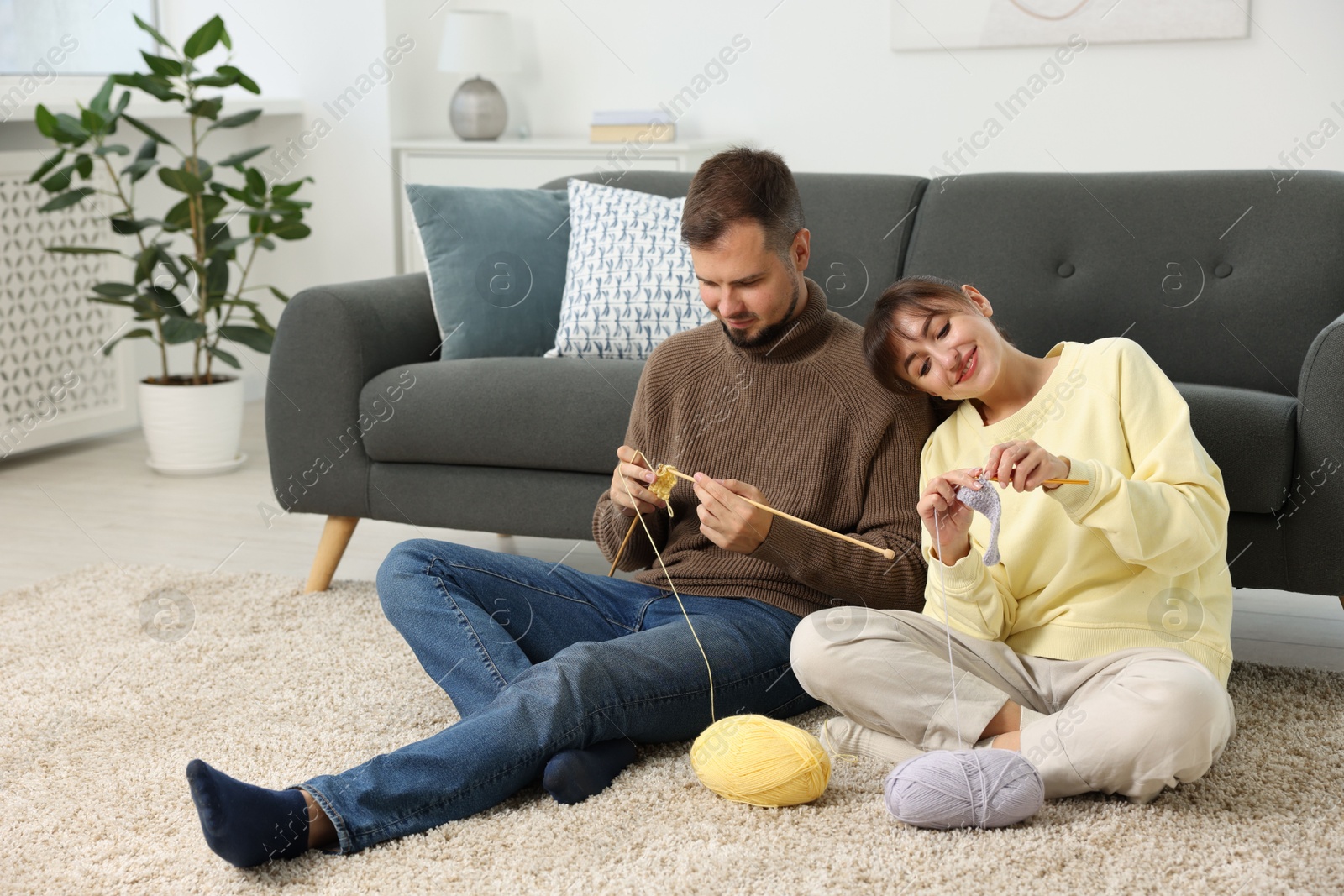 Photo of Woman teaching her boyfriend how to knit on floor at home