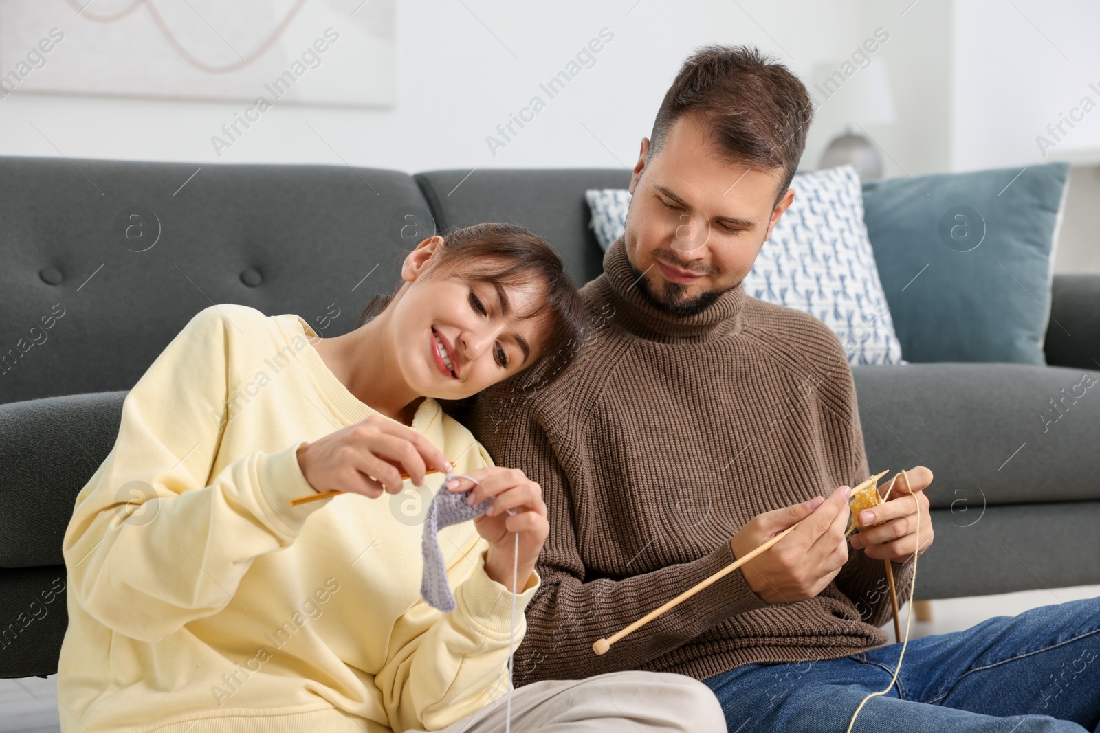 Photo of Woman teaching her boyfriend how to knit on floor at home