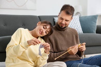 Woman teaching her boyfriend how to knit on floor at home