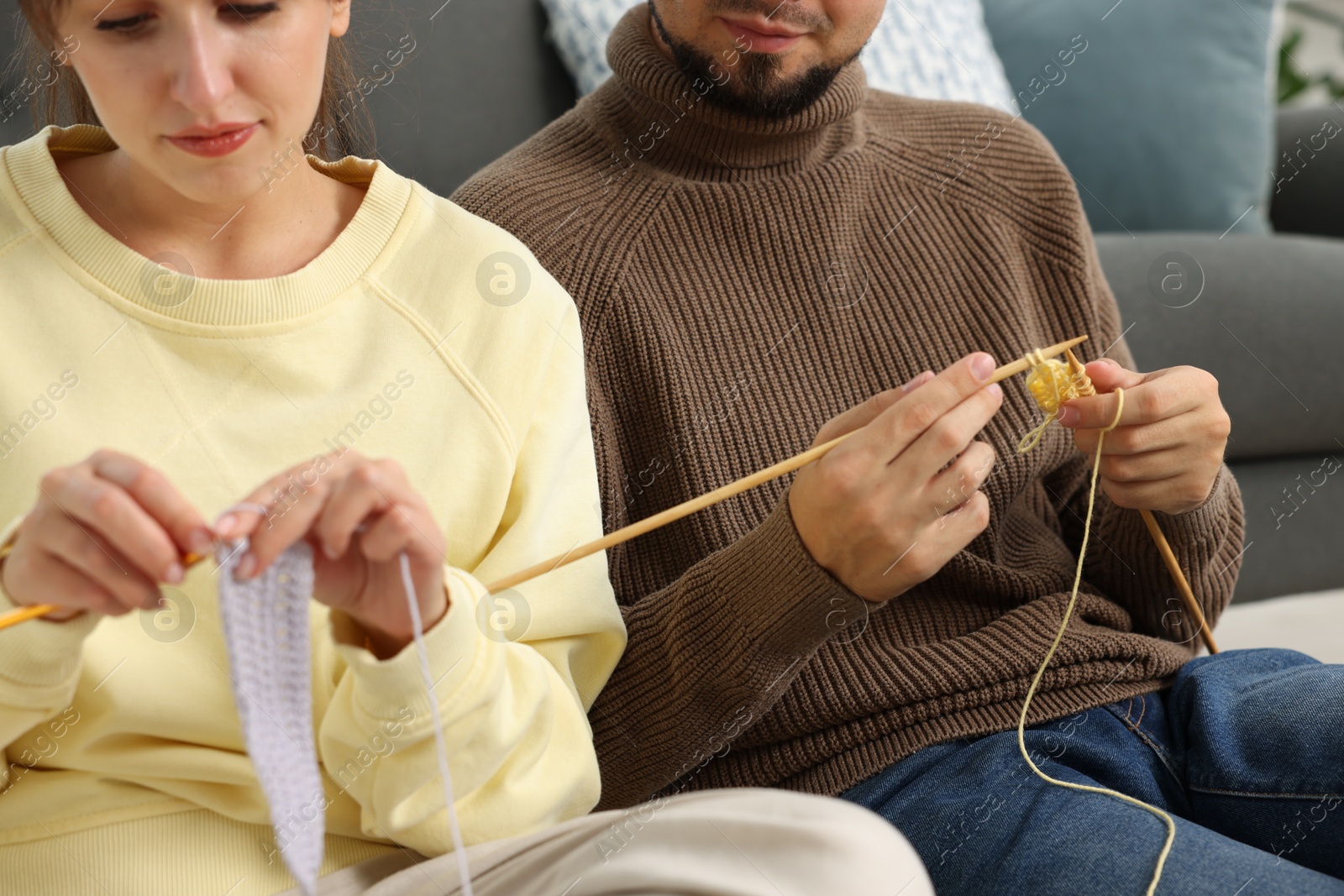 Photo of Woman teaching her boyfriend how to knit at home, closeup