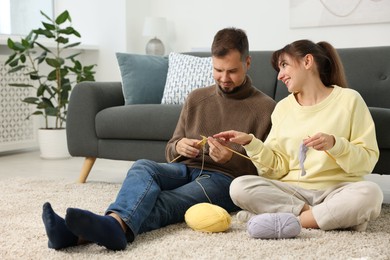 Woman teaching her boyfriend how to knit on floor at home