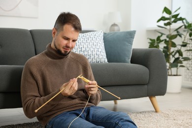 Man knitting with needles on floor at home