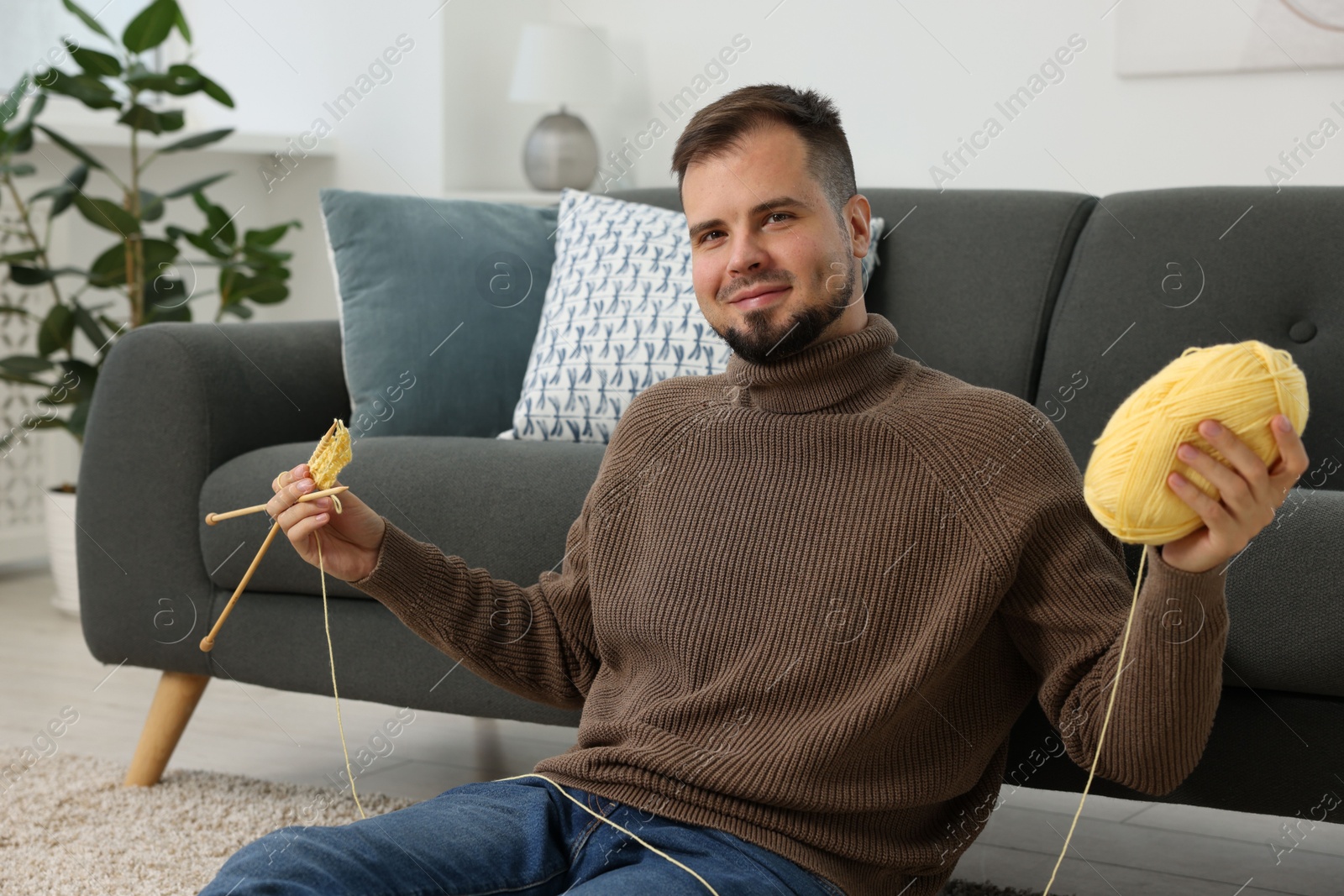 Photo of Man with yellow yarn and knitting needles on floor at home