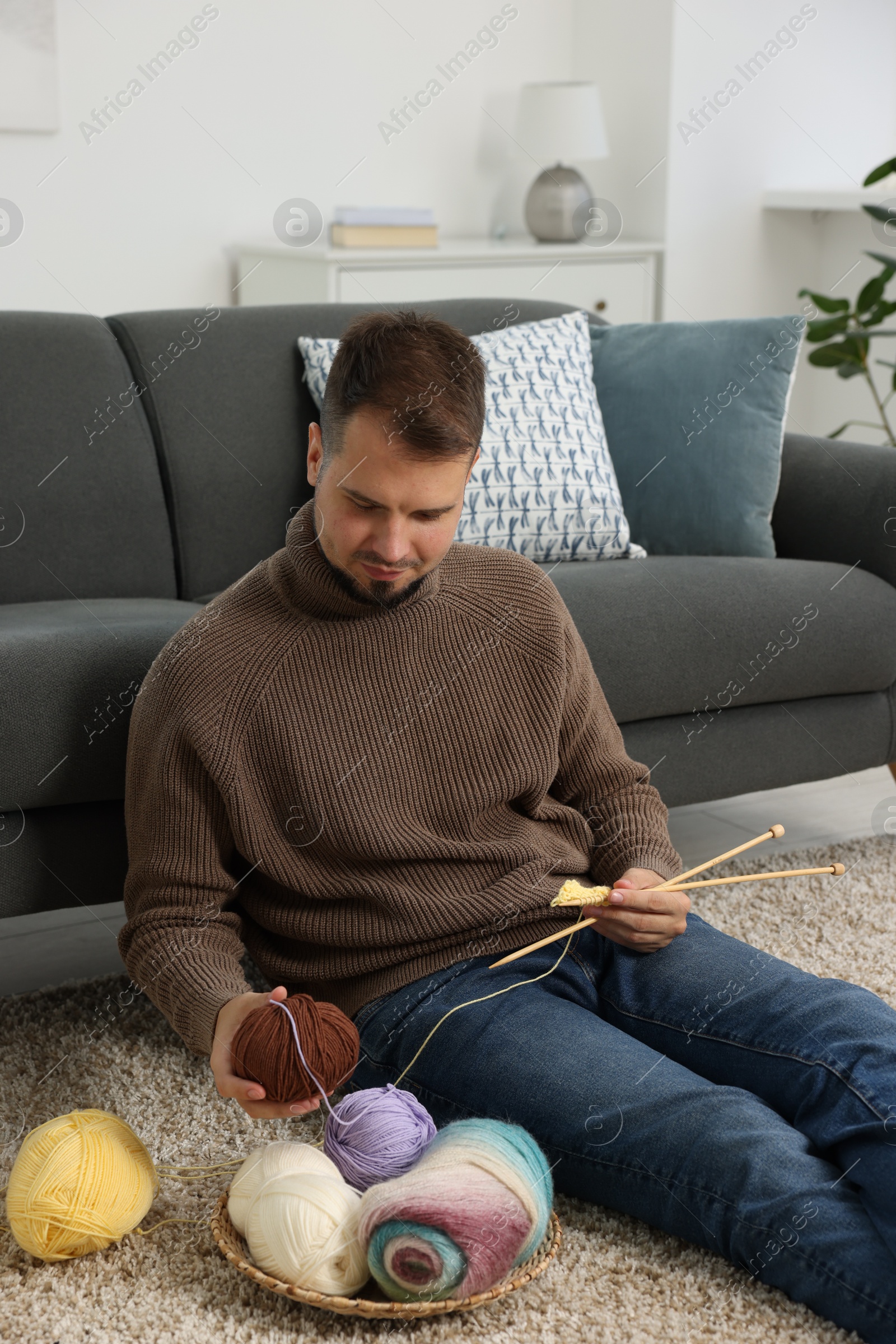 Photo of Man with colorful yarns and knitting needles on floor at home