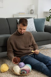 Man with colorful yarns and knitting needles on floor at home