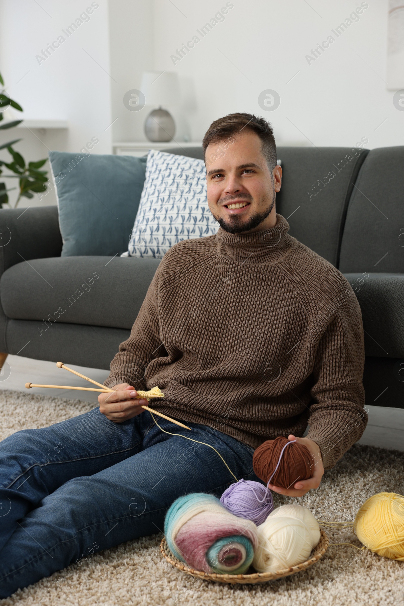 Photo of Man with colorful yarns and knitting needles on floor at home