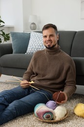 Man with colorful yarns and knitting needles on floor at home