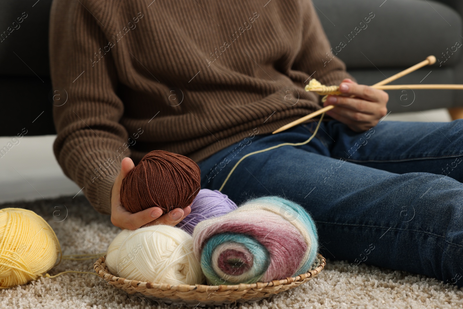 Photo of Man with colorful yarns and knitting needles on floor at home, closeup