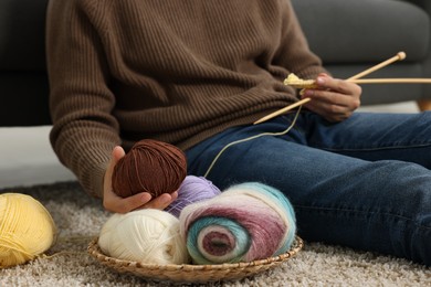 Man with colorful yarns and knitting needles on floor at home, closeup