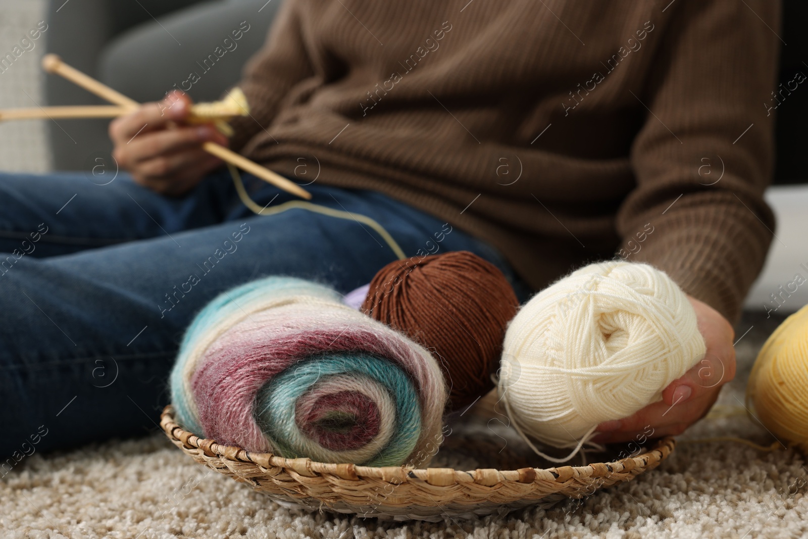 Photo of Man with colorful yarns and knitting needles on floor at home, closeup