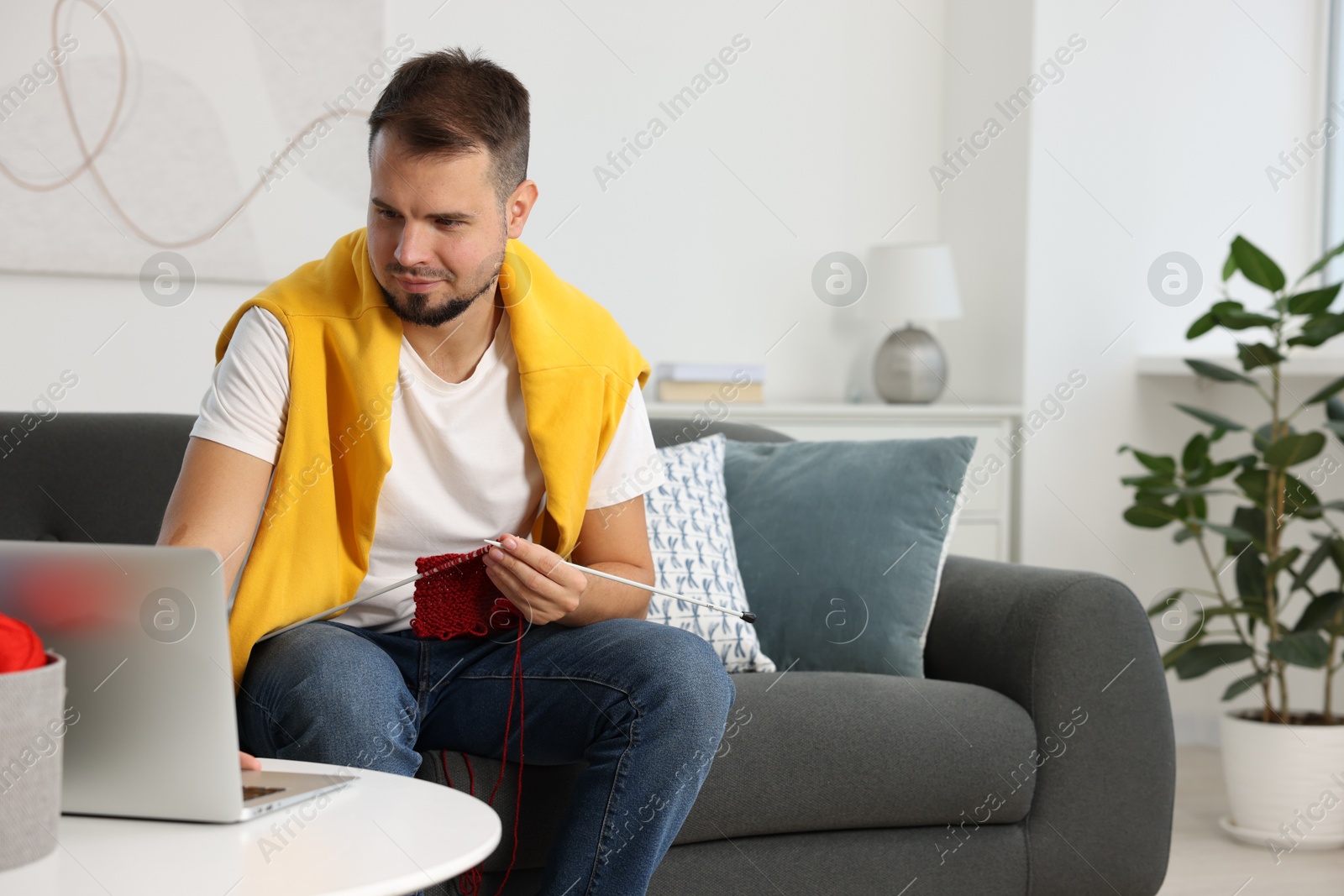 Photo of Man learning to knit with online course on sofa at home