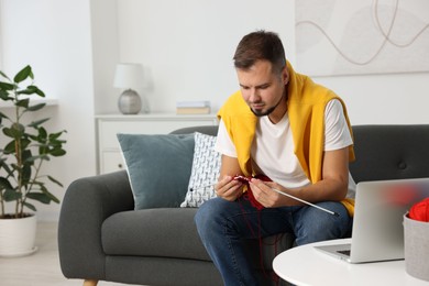 Man learning to knit with online course on sofa at home