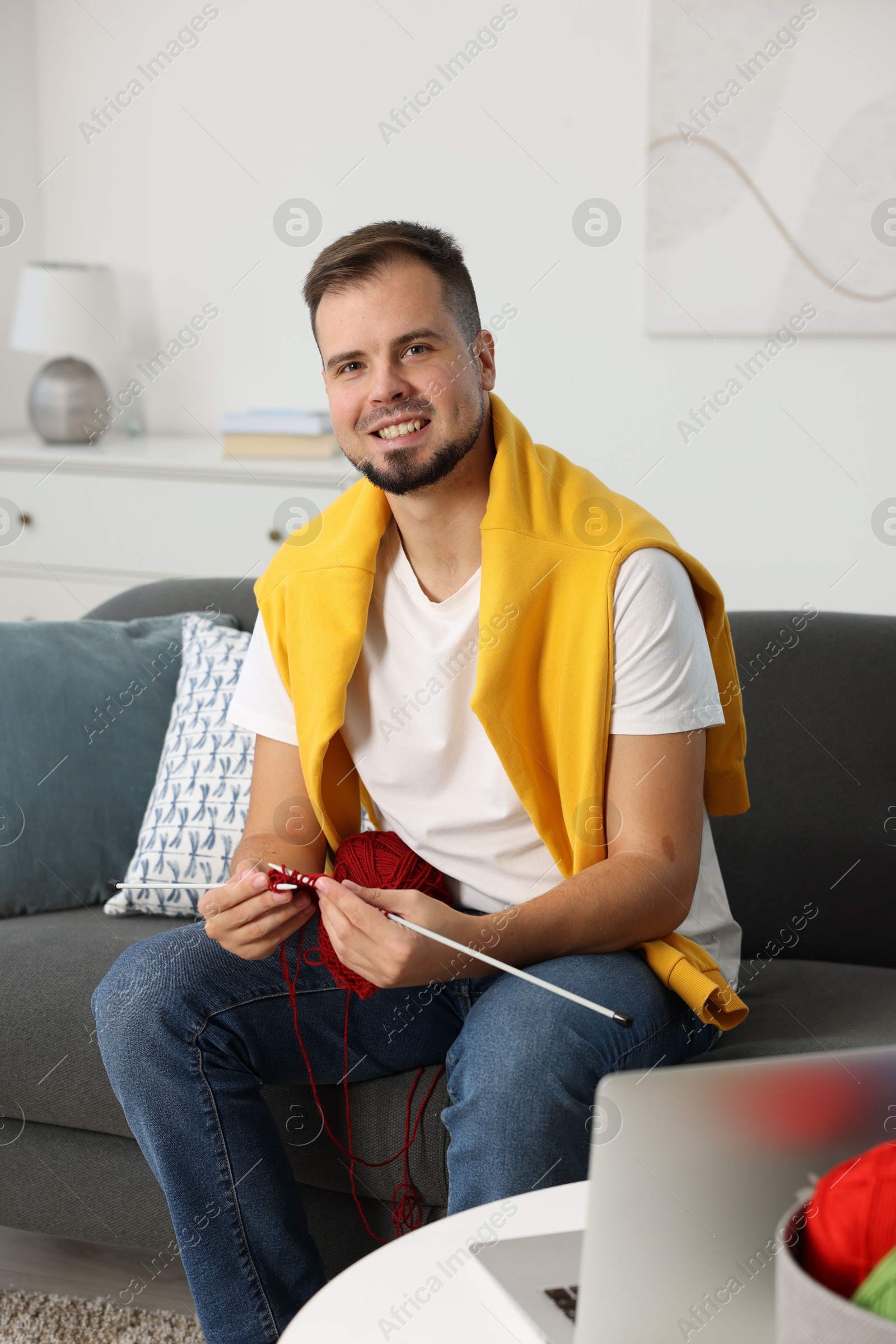 Photo of Man learning to knit with online course on sofa at home