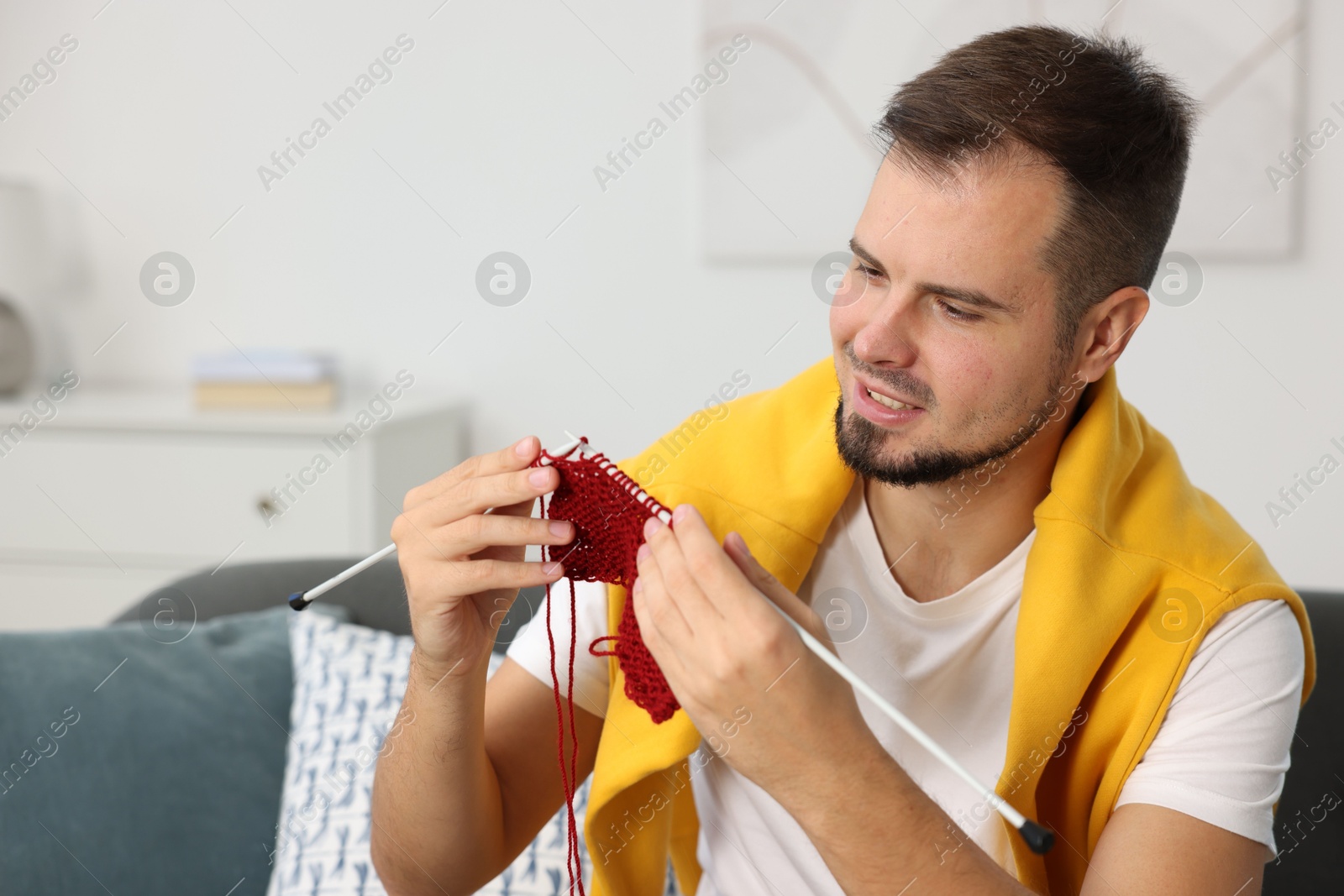 Photo of Man knitting with needles on sofa at home