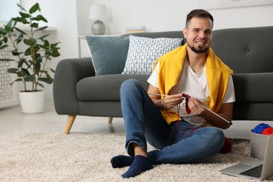 Man learning to knit with online course on floor at home