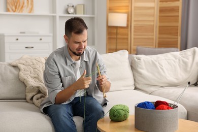 Man knitting with needles on sofa at home