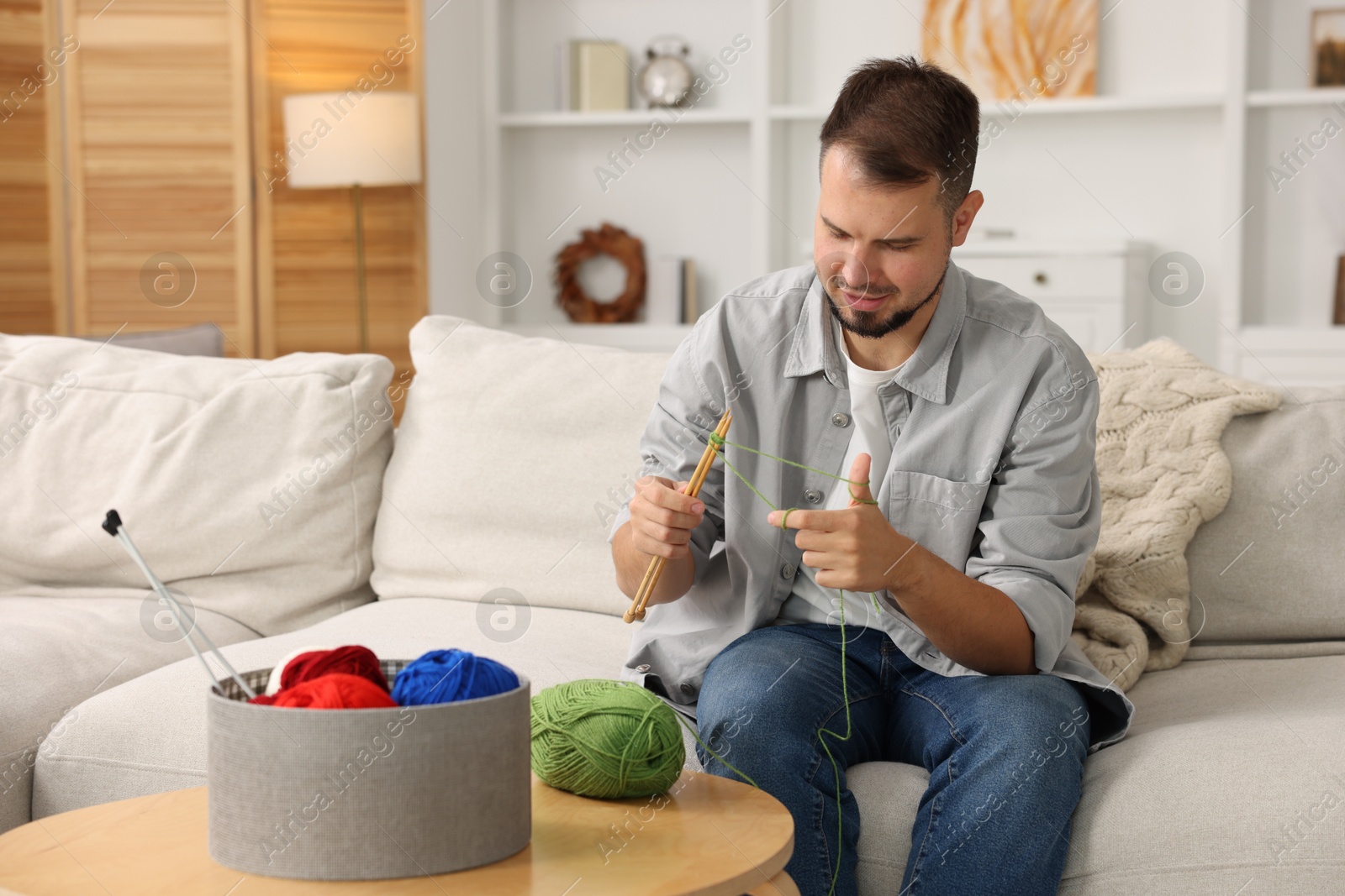 Photo of Man knitting with needles on sofa at home