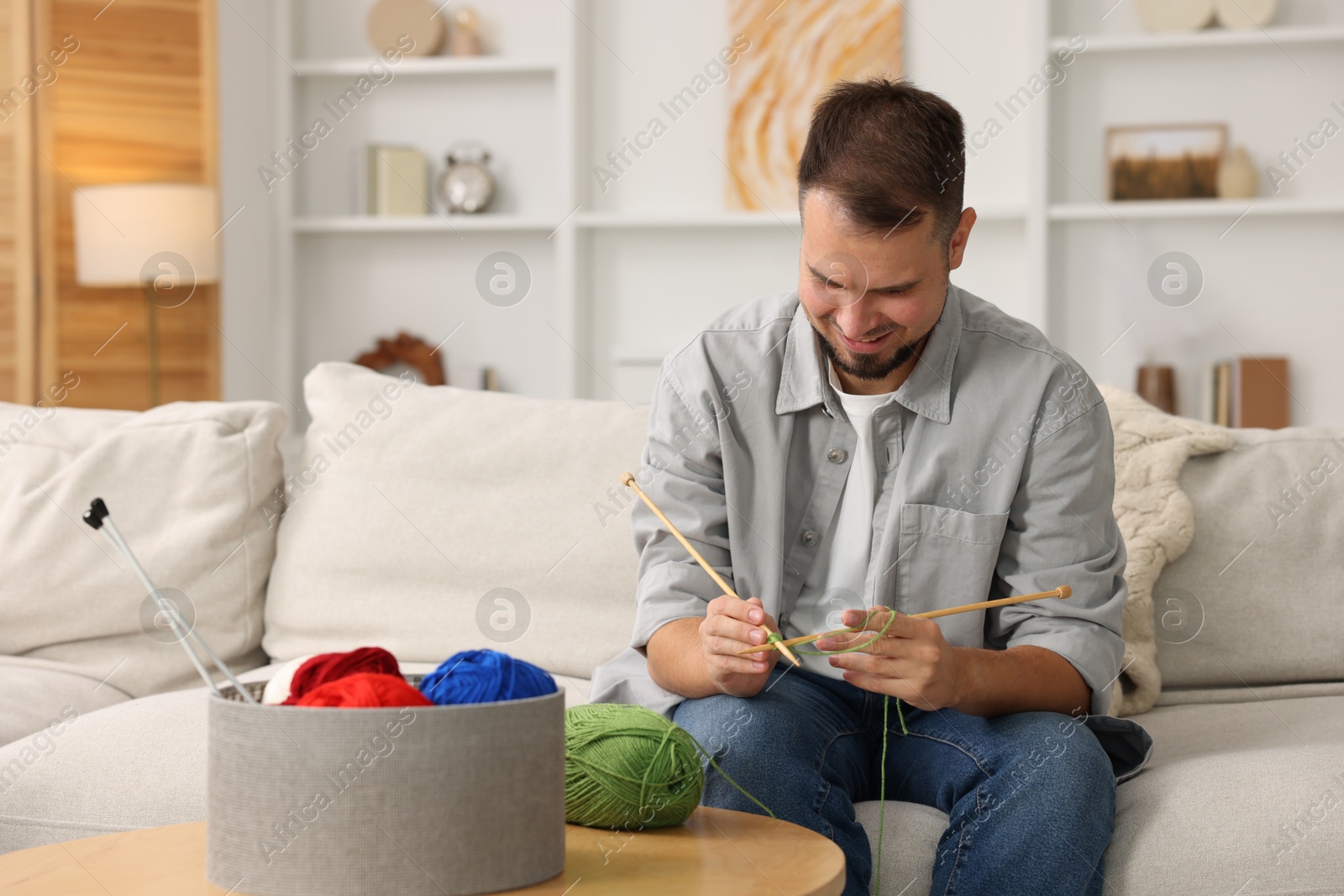 Photo of Man knitting with needles on sofa at home