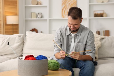 Man knitting with needles on sofa at home