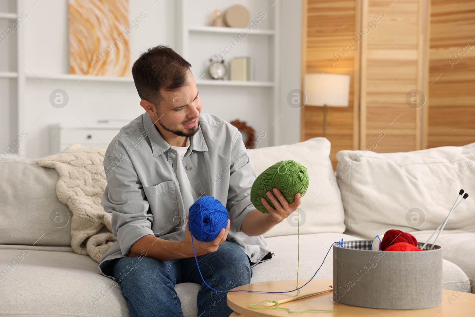 Photo of Man with colorful yarns on sofa at home. Knitting material