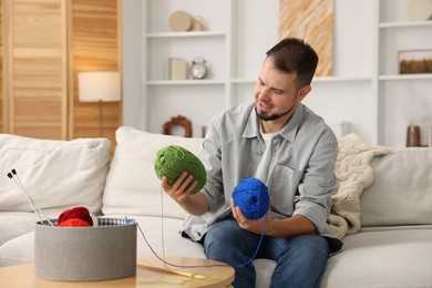 Man with colorful yarns on sofa at home. Knitting material