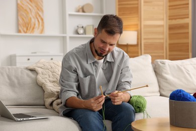 Man learning to knit with online course on sofa at home