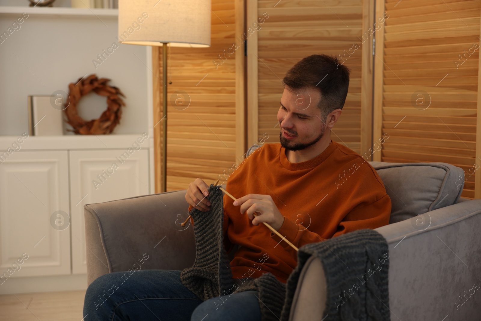 Photo of Man knitting with needles in armchair at home