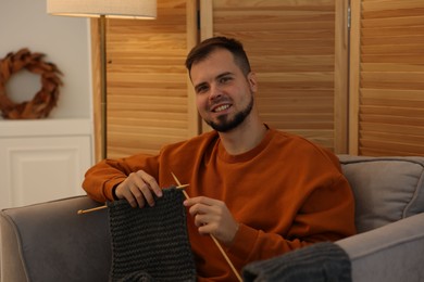 Photo of Man knitting with needles in armchair at home