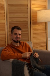 Man knitting with needles in armchair at home