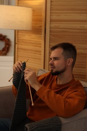 Photo of Man knitting with needles in armchair at home