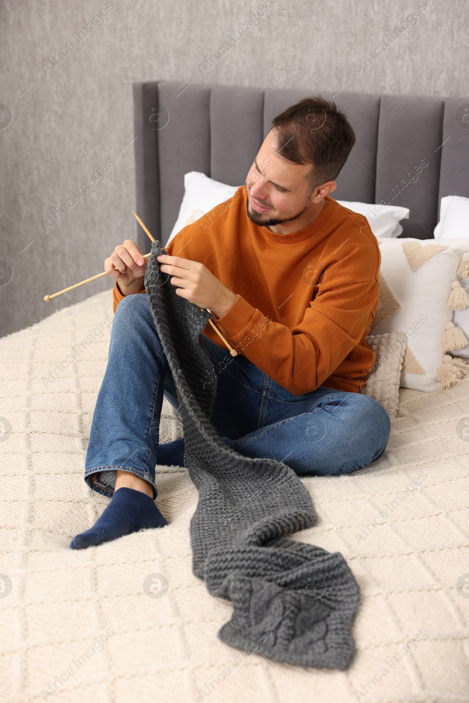 Photo of Man knitting with needles on bed at home