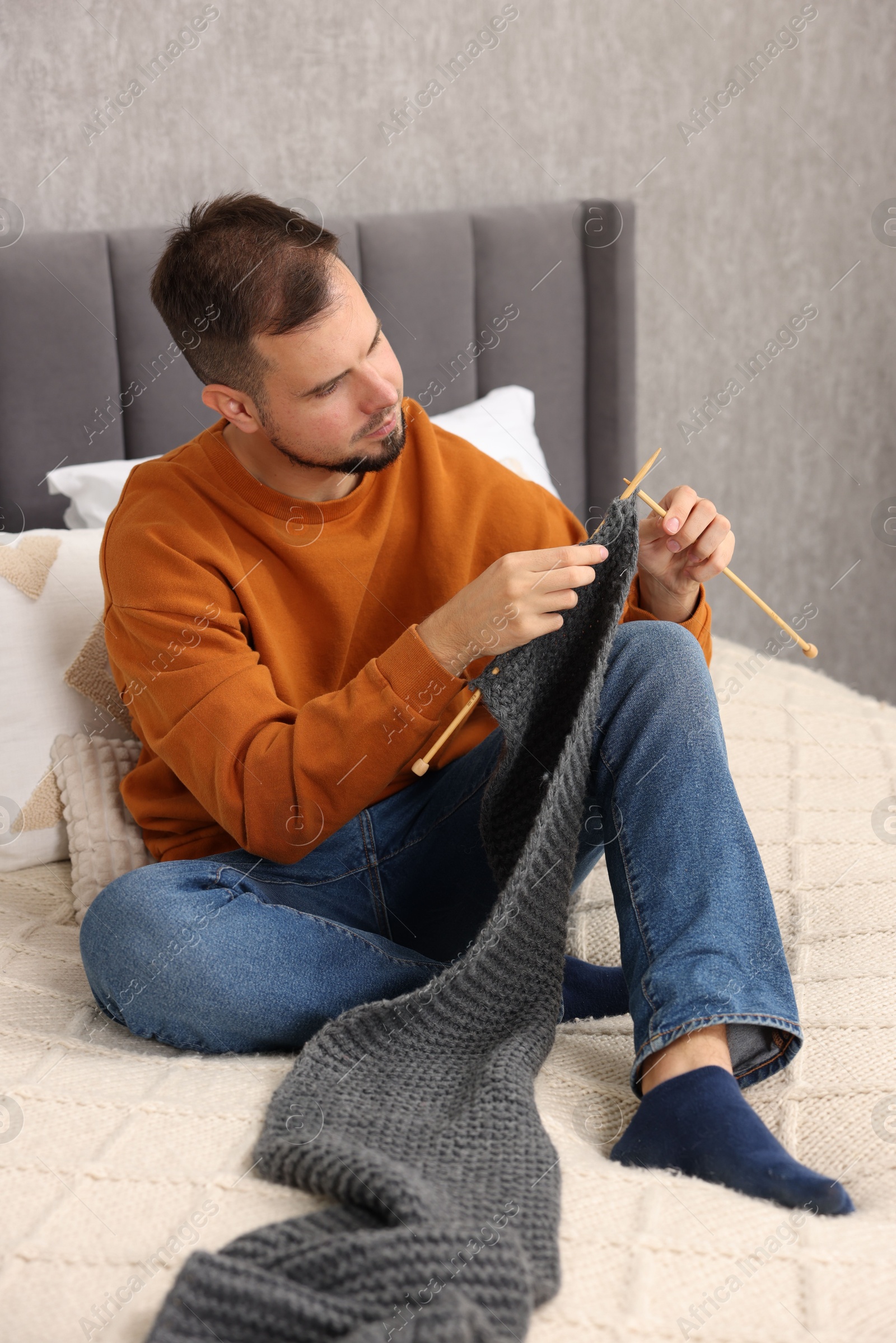 Photo of Man knitting with needles on bed at home