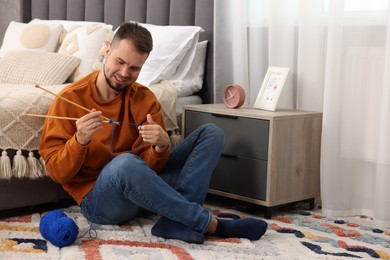 Man knitting with needles on floor at home