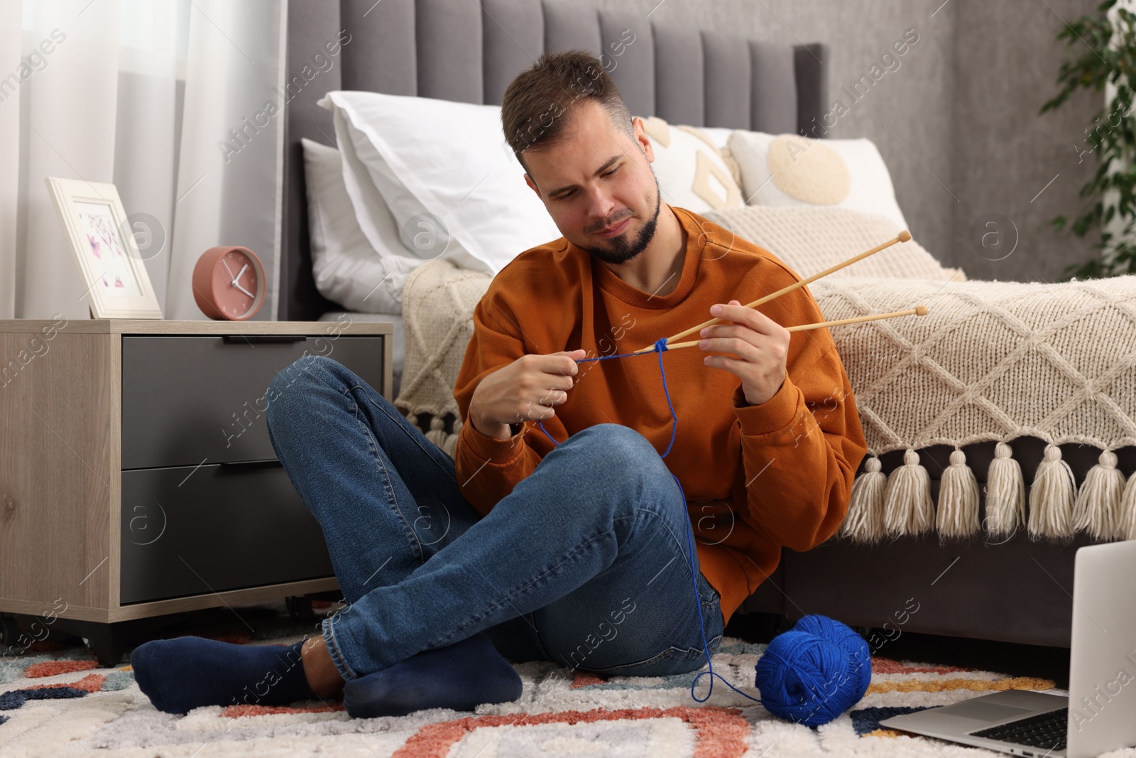 Photo of Man learning to knit with online course on floor at home